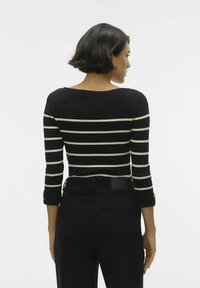 Must-valge triibuline ribikoes särk laia krae ja kolmeveerandi varrukatega, millel on kullatud nööbi aksessuaarid varrukaotstes. Mustad püksid.