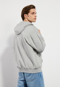 Grå hettegenser med snorhette, ribbestrikkede mansjetter og elastisk linning, paired med lyseblå denimjeans. Glatt tekstur og avslappet passform.