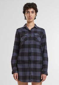 Camicia a maniche lunghe a quadri in cotone blu navy e nero. Presenta due tasche frontali, chiusura con bottoni e un design con colletto classico.