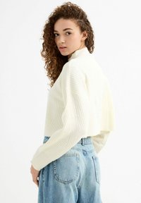 Suéter blanco de canalé con cuello alto y hombros caídos, combinado con jeans de mezclilla azul claro de tiro alto.