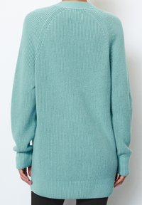 Long, light blue knit sweater with ribbed cuffs and hem. Features a textured weave and raglan sleeves, offering a relaxed fit.