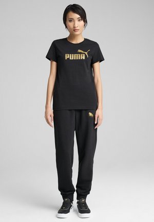 Sort bomulds t-shirt med guld "PUMA" logo, parret med sorte sweatpants med et guldlogo akcent og sorte sneakers med hvide såler.