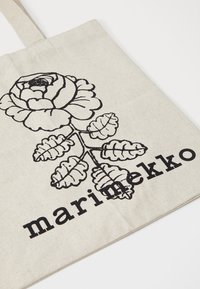 Canvas tote bag in natural beige with a black floral design featuring a rose and leaves, and the word "marimekko" in bold lettering.