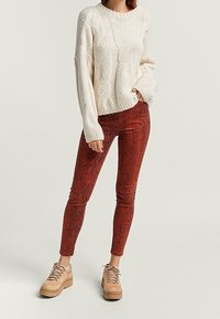 Licht crèmekleurige kabelgebreide trui, rode slangenprintlegging en tan kleurige veterschoenen met dikke zolen. Alle stukken hebben een casual, textuurlijke uitstraling.