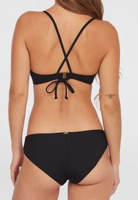 Set di bikini neri con design incrociato sulla schiena e legature regolabili. Tessuto liscio con copertura minima e una discreta accentuazione del marchio sul retro.