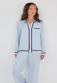 Lichtblauw pyjamaset met een lange mouwen top met knopen, marineblauwe accenten en een borstzak, gecombineerd met bijpassende broek met patroon.