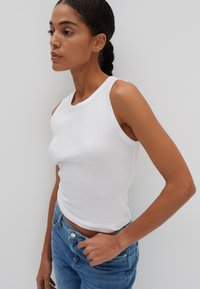 Top a righe bianco con silhouette aderente e scollatura ampia. Abbinato a jeans a vita alta di colore blu chiaro, con dettaglio a bottoni.