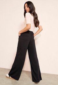 Fekete, széles szárú nadrág magas, elasztikus derékpánttal, két hátsó zsebbel és puha, texturált anyagból. Világos színű felsővel párosítva.