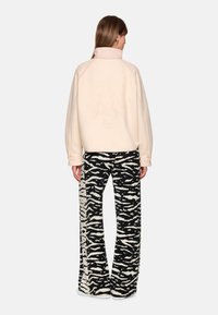 Cream-colored oversized sweatshirt with a high collar and embossed tiger design on the back, paired with black and cream zebra-print flared pants.