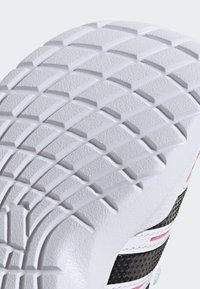 Semelle de chaussure en caoutchouc blanc avec motif de traction texturé, comportant des accents noirs et roses dans un design moderne. Accent mis sur les détails de la bande de roulement et les matériaux.