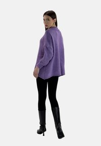 Fioletowy, oversize sweter z prążkowanym tekstem, długimi rękawami i wysokim kołnierzem. Zestawiony z czarnymi legginsami i czarnymi botkami do kolan.