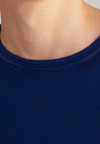 Gros plan sur le cou et le haut de la poitrine d'une personne portant un pull à col rond bleu marine.
