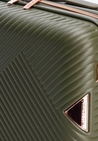 Valigia rigida verde oliva con texture a righe, zip in oro rosa e logo triangolare. Design robusto per l'uso in viaggio.