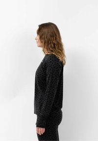 Schwarzes Langarmtop mit Leopardenmuster, weichem Material und tailliertem Design. Mit Daumenlöchern an den Bündchen akzentuiert.