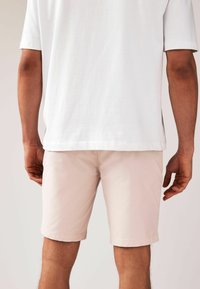 Shorts en coton rose clair avec un ourlet retroussé et des poches latérales, associés à un t-shirt blanc à manches courtes ample.