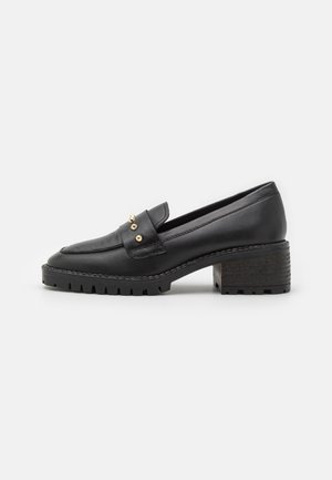 Mocassins en cuir noir avec clous dorés, talon bloc surélevé, semelle texturée antidérapante et finition lisse. Design classique avec des détails subtils.