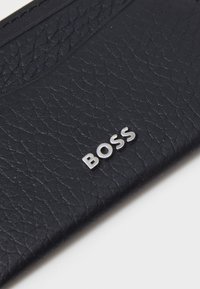 Portefeuille noir texturé en cuir avec un logo "BOSS" argenté à l'avant, présentant une finition lisse et un design simple.
