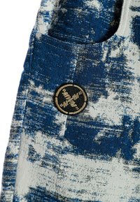 Tela azul y blanca con un patrón y un parche que presenta un logo circular. Incluye un bolsillo con detalles de costura visibles.