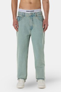 Light blue, loose-fitting jeans with a faded finish. Features a button front and belt loops. Styled with white sneakers and visible waistband.