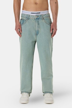 Light blue, loose-fitting jeans with a faded finish. Features a button front and belt loops. Styled with white sneakers and visible waistband.