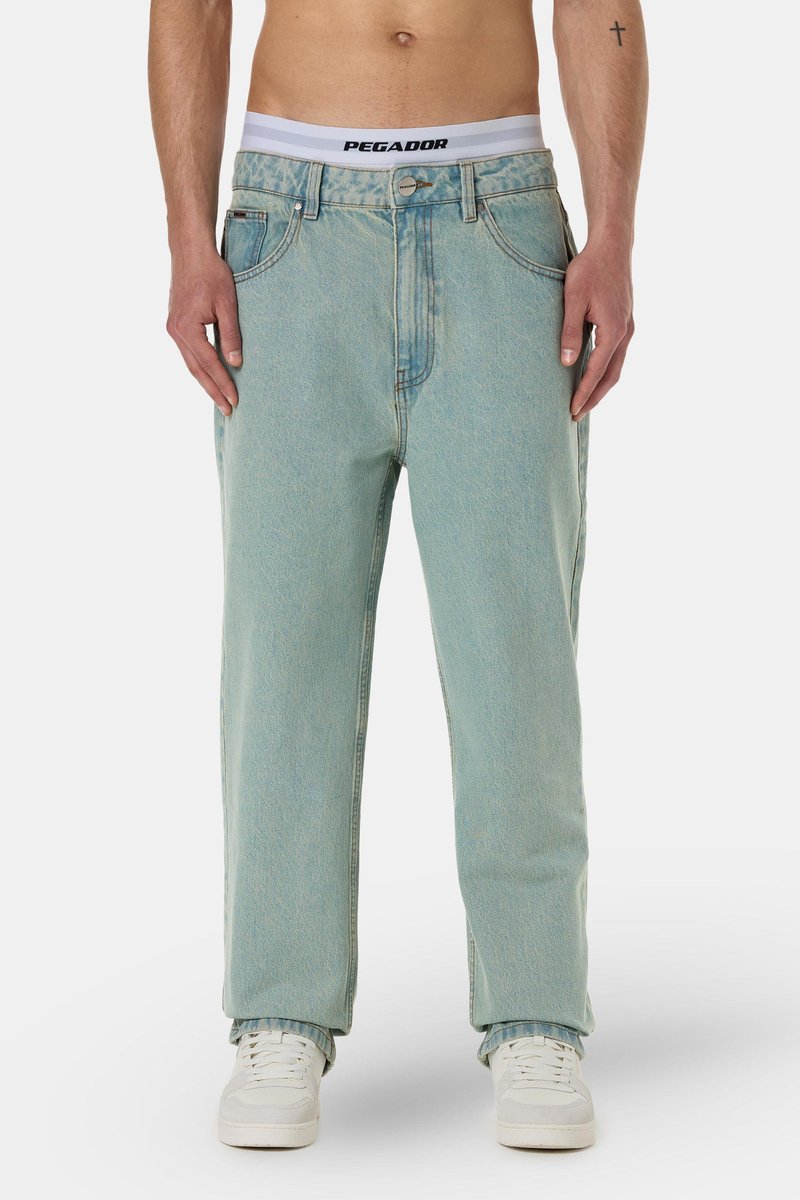 Light blue, loose-fitting jeans with a faded finish. Features a button front and belt loops. Styled with white sneakers and visible waistband.