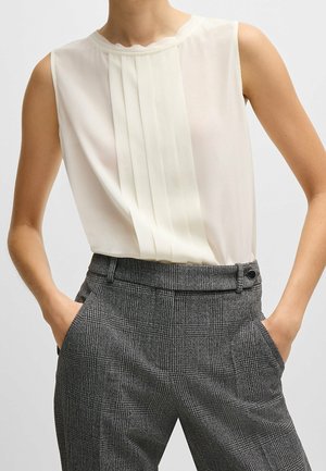 White sleeveless blouse with pleats at the front, paired with gray plaid trousers featuring side pockets and a button detail.