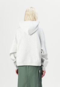 Gray hooded sweatshirt with dropped shoulders, ribbed cuffs, and hem, paired with a green skirt featuring side pockets. Smooth texture.
