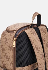 Rucsac maro cu model, exterior texturat, panouri laterale din plasă, fermoar auriu și mâner superior pentru transport.