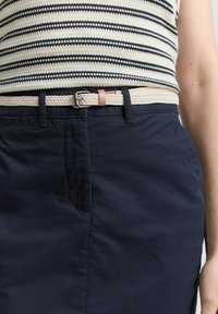 Navyblauwe rok met een gestructureerde, geweven beige riem met een zilveren gesp. De rok heeft voorzakken en een gladde afwerking.
