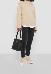 Pull à col roulé en maille beige, pantalon en coton noir, bottines beiges à lacets, et sac à main en cuir noir avec des accents de quincaillerie dorée.