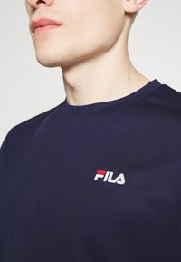 Camiseta Fila de color azul marino con cuello redondo y un tejido texturizado. Presenta un logo blanco con acentos rojos en la zona del pecho izquierdo.