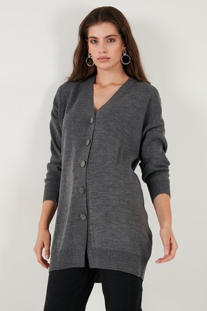 Cardigan gris avec un col en V, des manches longues et six boutons de fermeture. Texture en tricot douce, légèrement plus longue à l'arrière, design minimaliste.