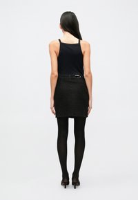 Černá pletená mini sukně s texturovaným vzorem, doplněná černým tílkem. Outfit je dokončen průhlednými černými punčochami a lodičkami.