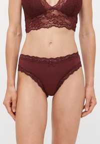 Burgunderfarget blonde bralette med bølgete kanter og en sløyfedetalj, paired med matchende høytlivsundertøy med blondedetaljer langs linningen.
