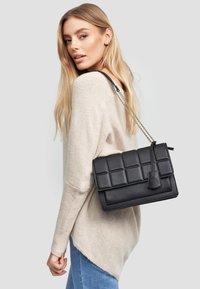 Czarna pikowana torebka wykonana ze skóry, z łańcuszkowym paskiem i zapięciem na klapkę. Torebka ma zorganizowany kształt i gładką teksturę.