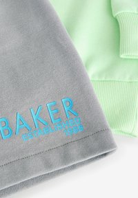Grijs stof met blauwe tekst "BAKER" en detail "OPGERICHT 1988", naast een mintgroene gestructureerde stofsegment.