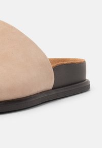 Atviros nosies sandalai iš minkštos kreminės suedes su korko padu. Yra juodas gumos padas ir išlenkta viršutinė dalis, užtikrinanti komfortą.