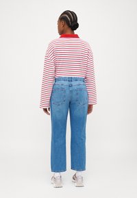 Striped long-sleeve shirt with red collar, paired with light blue straight-leg jeans. Grey sneakers with white soles. Textured fabric.