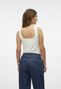 Débardeur blanc sans manches avec un dos carré, accompagné d'un jean large bleu foncé avec une taille lisse et des poches arrière.