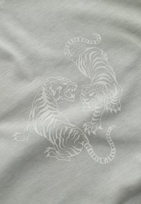 Hellgrauer Stoff mit einem Druck von zwei weißen Tigern mit detaillierten Streifen, die sich gegenüberstehen, vor einer glatten Textur.