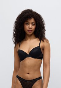 Μαύρο σουτιέν από δαντέλα και δίχτυ με ενισχυμένα cup, κυματιστά άκρα και λεπτές ρυθμιζόμενες τιράντες. Συνδυασμένο με αντίστοιχο εσώρουχο από δαντέλα.