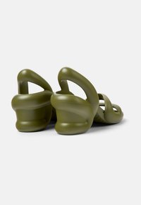Green, molded rubber sandals featuring a distinctive wave-like design, cut-out straps, and a contoured sole for added comfort and style.