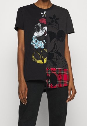 Person iført en sort T-shirt med korte ærmer med et delt vintage Mickey Mouse-grafik og en rød ternet lap på nederste højre side.