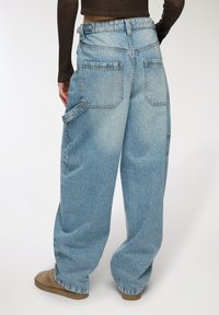 Pantaloni cargo in denim blu chiaro con vestibilità comoda, dotati di molteplici tasche e cuciture a vista. La vita è chiusa con una cerniera.