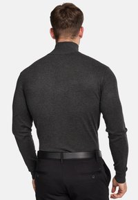 Mørk grå, langærmet turtleneck sweater med et struktureret strikkemønster, der har en tætsiddende pasform og en høj krave. Bæret sammen med sorte bukser.