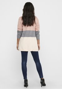 Stickad tröja med långa ärmar, med horisontella ränder i mjuk rosa, grå och krämfärg. Bärs över mörka skinny jeans och ankelboots.