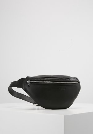 Czarna skórzana nerka z srebrnym zamkiem i regulowanym paskiem, prezentowana na białym podeście na tle szarej, gładkiej ściany.