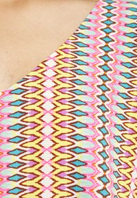 Tecido colorido e padronizado com linhas em ziguezague nas cores rosa, azul, amarelo e castanho. Textura suave com um design geométrico vibrante.