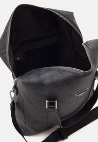 Sac texturé noir avec ferrures argentées, comprenant une ouverture zippée, une poche intérieure en maille et une sangle réglable. Motif logo à l'extérieur.