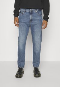 Blå jeans i denim med rak passform, fem-ficksdesign, subtil blekning och silverdetaljer. Kombinerade med svarta skor med gula accenter.